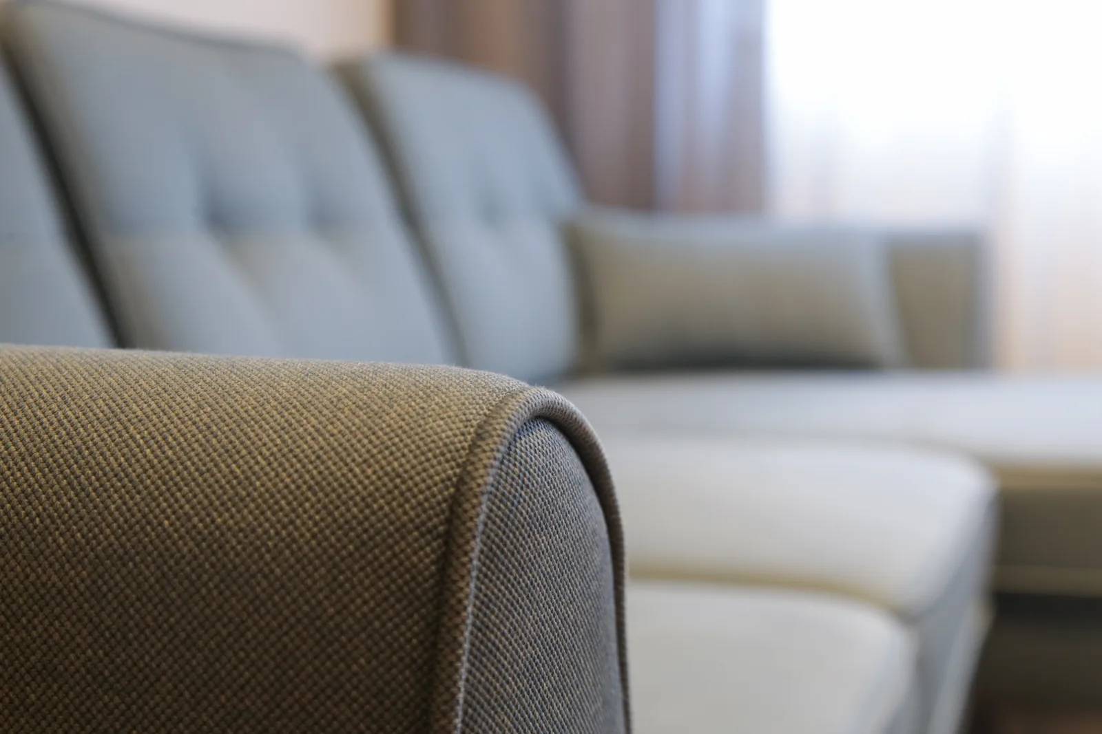 Close-up of a woven fabric sofa arm with a tufted upholstered sofa behind it, showing the different upholstery fabrics R&L Carpet Cleaning cleans in Kansas City homes